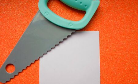 toy tools, saw, bolts and nuts on an orange background. white sheet of paper place for textの写真素材