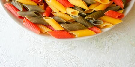 multi-colored pasta in a plate on a white table. beautiful colored pasta lie in a plate as a background, place for textの写真素材