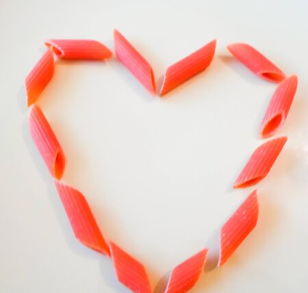 multi-colored pasta in plates in the form of a heart on a white table. beautiful colored pasta lie in a plate in the shape of a heart, place for text. love conceptの写真素材