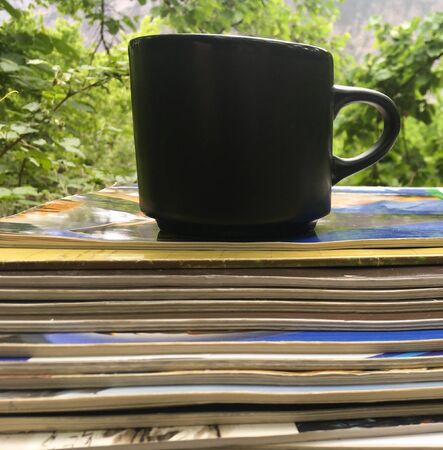 a stack of fresh morning Newspapers and a Cup of coffee against a background of greenery. A Cup of hot coffee and Newspapers in the garden in the morningの写真素材