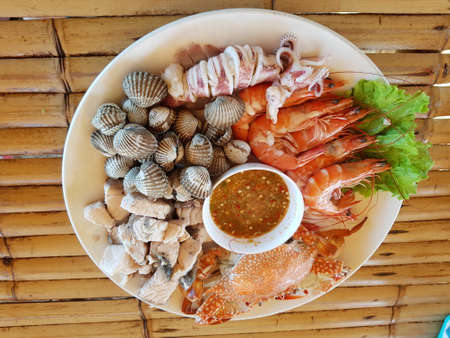Seafood, including shrimp, fish, cockles, squid, squid, along with spicy dipping sauce on a plate placed on a bamboo table.の写真素材
