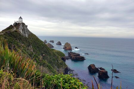 The Nugget Point Lighthouse at a stormy day with the cliff and boulders in the seaの写真素材