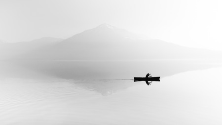 Fog over the lake. Silhouette of mountains in the background. The man floats in a boat with a paddle.の写真素材