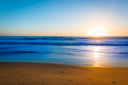 Sand beach with traces of footprints and ocean surf is painted in the colors of the setting sun. Coast of California.の写真素材