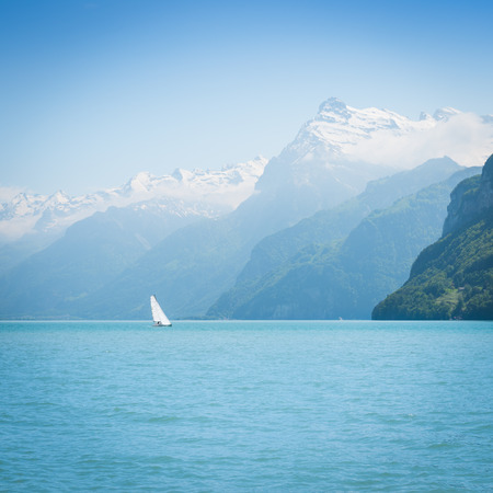 Grandiose mountain landscape. Mountain tops in the snow. White sail on a romantic lake.の写真素材