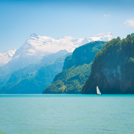 Grandiose mountain landscape. Mountain tops in the snow. White sail on a romantic lake.の写真素材