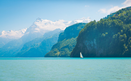 Grandiose mountain landscape. Mountain tops in the snow. White sail on a romantic lake.の写真素材