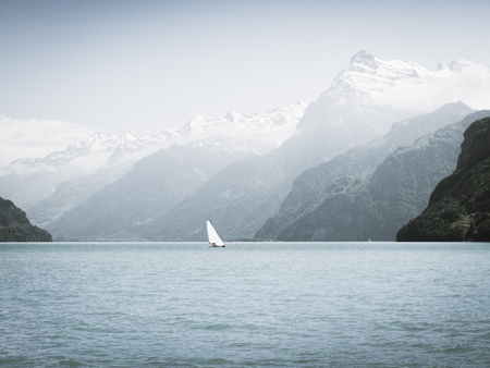Grandiose mountain landscape. Mountain tops in the snow. White sail on a romantic lake.の写真素材