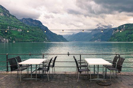 Cafe on the lakeside promenade. Wicker chairs and tables. Garland festive lights hanging from the top.のeditorial素材