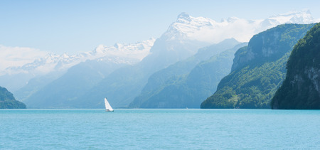 Grandiose mountain landscape. Mountain tops in the snow. White sail on a romantic lake.の写真素材