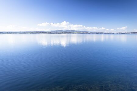 Lake Zug in central Switzerland. Clouds are reflected in water lake. At the edge water is clear and...