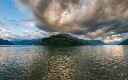 Thundercloud painted in red. Dramatic and heavy sky over lake and mountainsの写真素材
