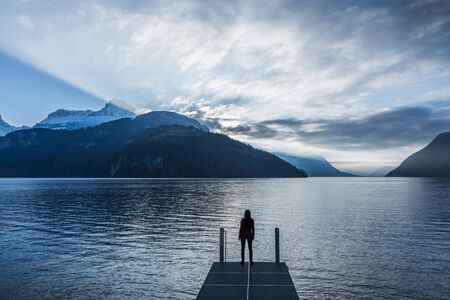 epic landscape complete with a small woman figure. Mountain, lake and sky in bright colors of sunsetの写真素材