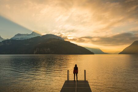 epic landscape complete with a small woman figure. Mountain, lake and sky in bright colors of sunsetの写真素材
