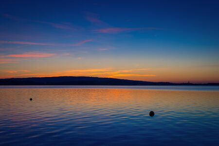 The setting sun painted the sky and the lake in bright colors. Clouds and drawings in the sky reflected in the waterの写真素材