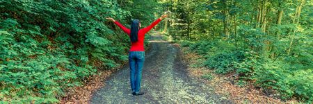 Woman in the forest on the edge. She raised her hands up in an appeal to nature. Sun rays in the trees. Further prospects of the road.の写真素材