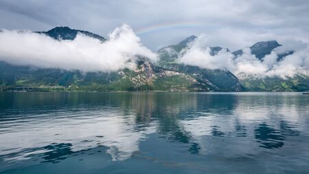 Mountain landscape in the clouds. Mountain lake reflects the sky and rainbow. Switzerland.の写真素材