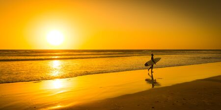 Surfer with board on the sand beach Oceana. Bright sunset on the horizon.