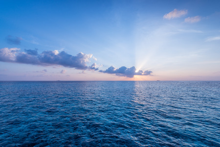 Sunset over ocean. On the horizon, the sun's rays shine through the cloudsの写真素材