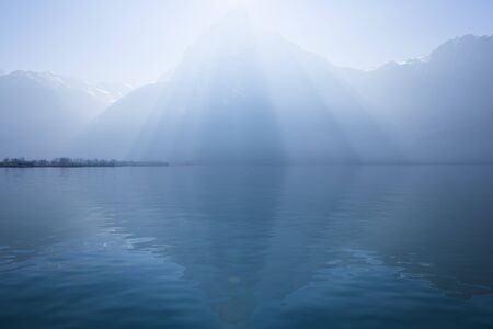 Sunrays over the top of the mountains reflected in the lake. Play of light and shadow creates volume pyramid shape in nature.の写真素材