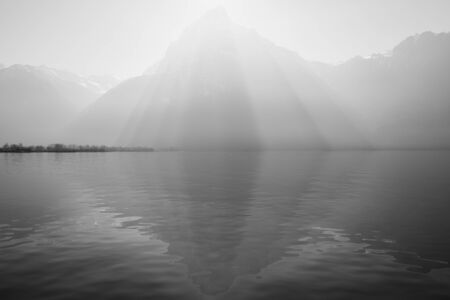 Sunrays over the top of the mountains reflected in the lake. Play of light and shadow creates volume pyramid shape in nature.の写真素材