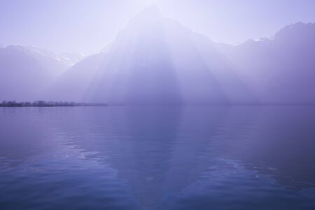 Sunrays over the top of the mountains reflected in the lake. Play of light and shadow creates volume pyramid shape in nature.の写真素材