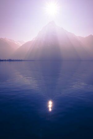 Sunrays over the top of the mountains reflected in the lake. Play of light and shadow creates volume pyramid shape.の写真素材