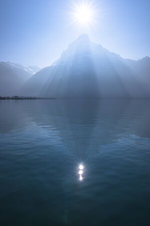 Sunrays over the top of the mountains reflected in the lake. Play of light and shadow creates volume pyramid shape.の写真素材