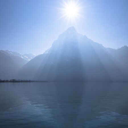 Sunrays over the top of the mountains reflected in the lake. Play of light and shadow creates volume pyramid shape.の写真素材