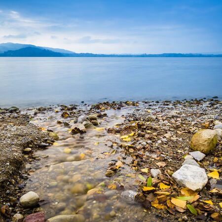 Autumn landscape on the lake. On the shore are colored stones and fallen leaves.の写真素材