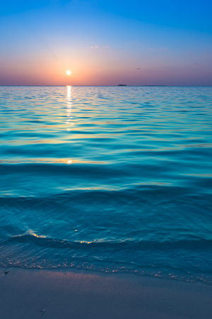 Fantastic color of sunset on a tropical island. Waves on the white sand beach. Relax evening in the Maldives.の写真素材