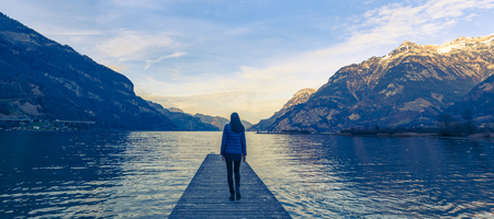 Woman goes on a wooden pier. Lake between the mountain ranges. Mountain landscape in the evening.の写真素材