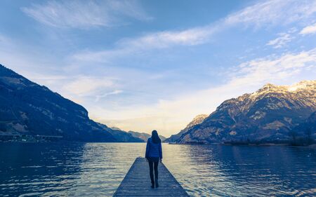 Woman goes on a wooden pier. Lake between the mountain ranges. Mountain landscape in the evening.の写真素材