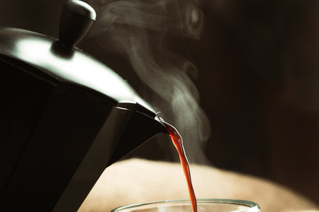 Pouring hot coffee from a kettle into a glass, close upの写真素材