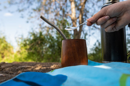 Close up of a woman's hand pouring water into a wooden cup on a picnic table