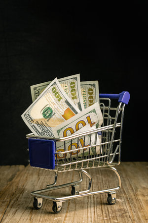 Shopping cart with dollar banknotes on a wooden table, black backgroundの写真素材