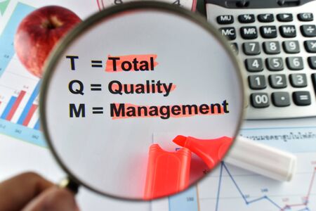 magnifier on meaning of TQM with document, calculator and marker., for business concept