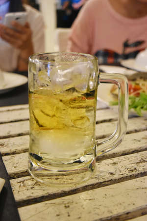 Glass of beer with ice on wooden table in restaurantの写真素材