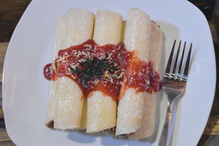 Roll pancakes with berries fruit sauce and fork on white plate in restaurant.の写真素材