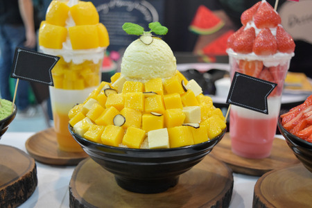 Korean shaved ice cream dessert with sweet toppings, Mango Bingsu or Bingsoo with fresh milk and whipping cream in korea style on black cup.の写真素材