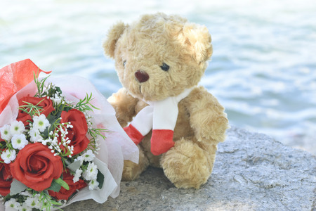Cute Teddy bear with red roses bouquet on old stone and sea background. concept of love Valentine's Day, Friendship, Family and Wedding.の写真素材