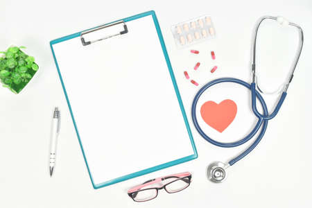 Top view of doctor desk table with stethoscope, eyeglass, drug and blank paper on clipboard and pen. Top view with copy space.の写真素材