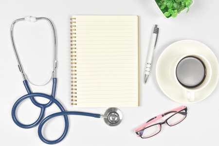 Medical mock-up with blank notebook, stethoscope, glasses, cup of coffee on doctor desk. Top view. copy space.の写真素材