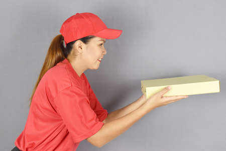 Delivery concept. Delivery woman holding pizza box for customer services on grey background.の写真素材