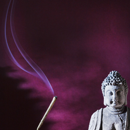 stone sitting buddha and frankincense, red backgroundの写真素材