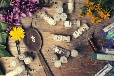 bottles with homeopathy globules and spoon, decorated with flowers pinks and ivyのeditorial素材