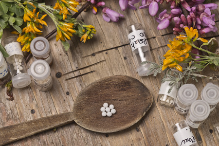bottles with homeopathy globules and spoon, decorated with flowers pinks and yellowのeditorial素材