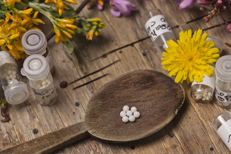 bottles with homeopathy globules and spoon, decorated with flowers pinks and yellowのeditorial素材