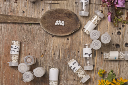 bottles with homeopathy globules and spoon, decorated with flowers pinks and yellowのeditorial素材