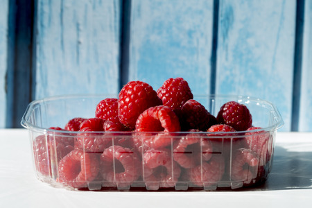 Raspberries in a plastic box on a blue wooden backgroundの写真素材